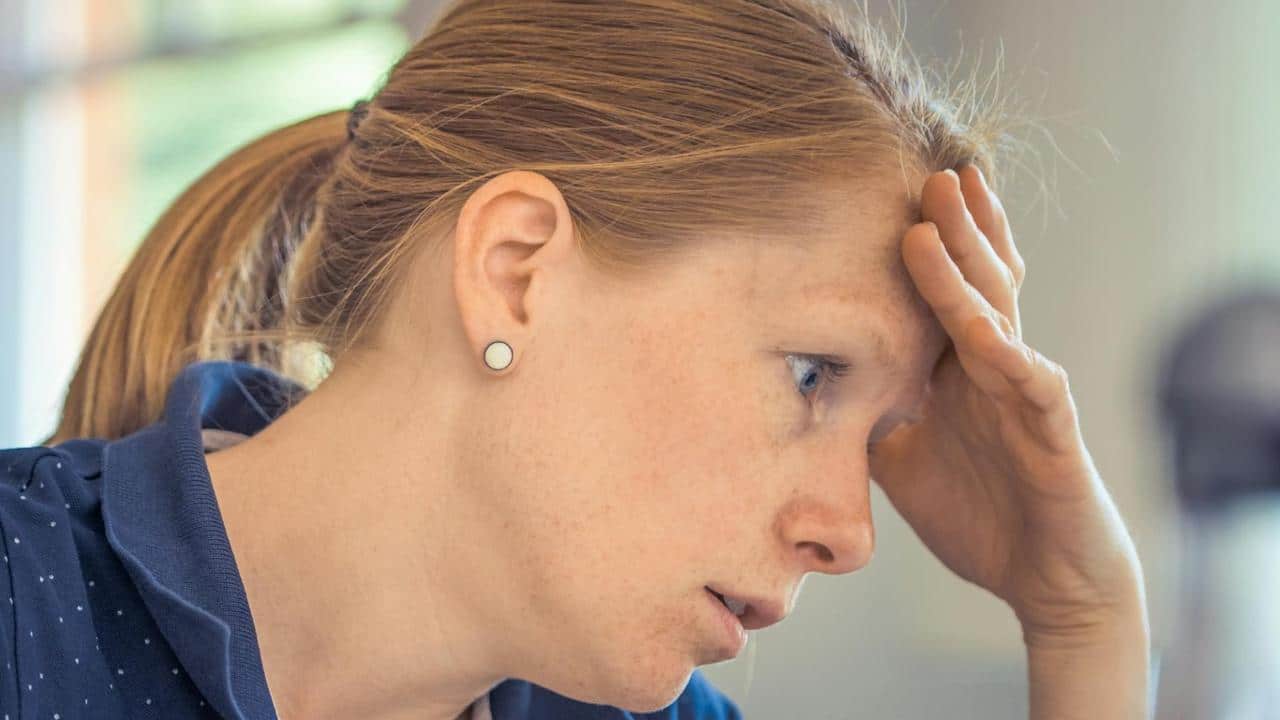 Femme fatiguée tenant sa tête, illustrant les effets de la ménopause précoce sur la santé cardiovasculaire