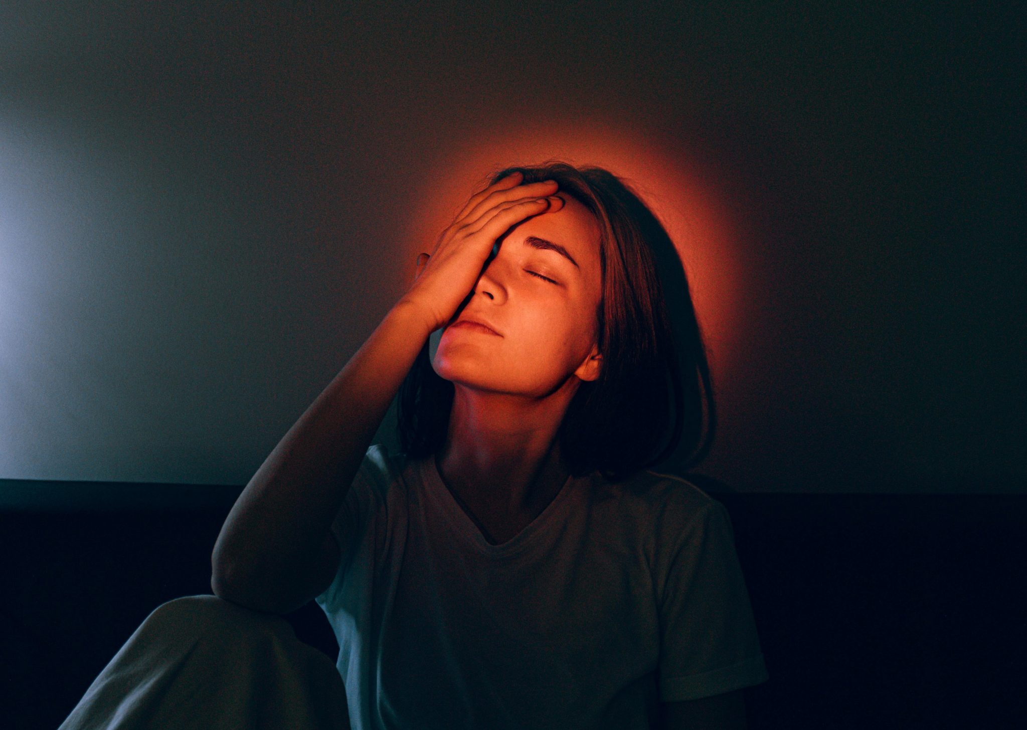 Femme souffrant d’une migraine, main sur le front, illustrant la douleur et la sensibilité à la lumière