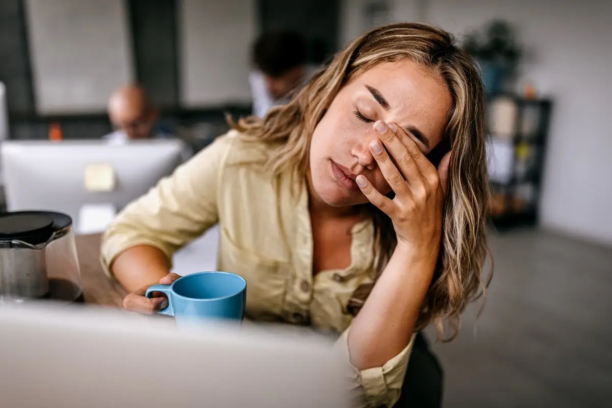Femme fatiguée au travail tenant une tasse de café, illustrant l’épuisement et la fatigue chronique
