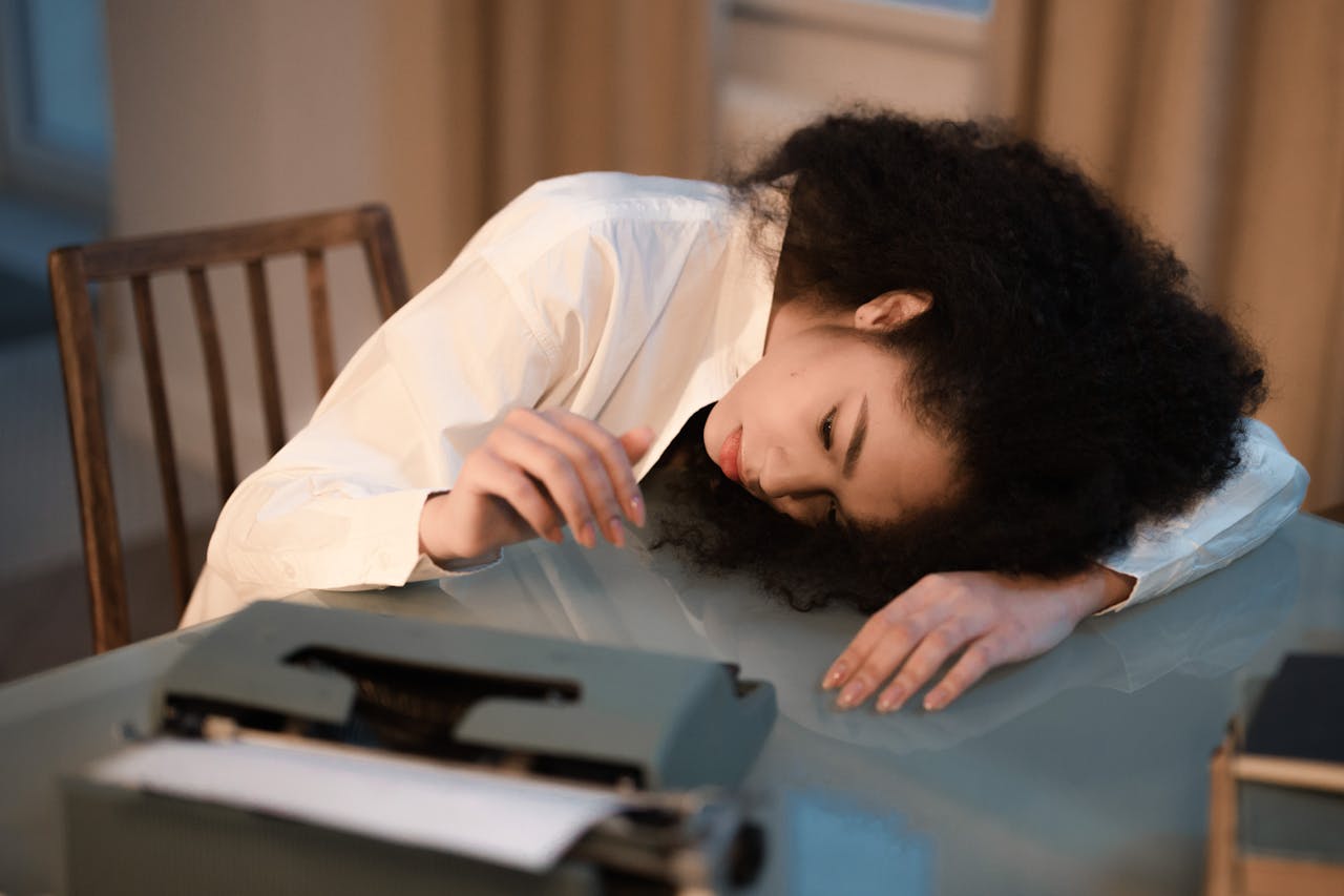 Femme fatiguée endormie sur un bureau, illustrant le manque de sommeil et l’épuisement lié à la dette de sommeil