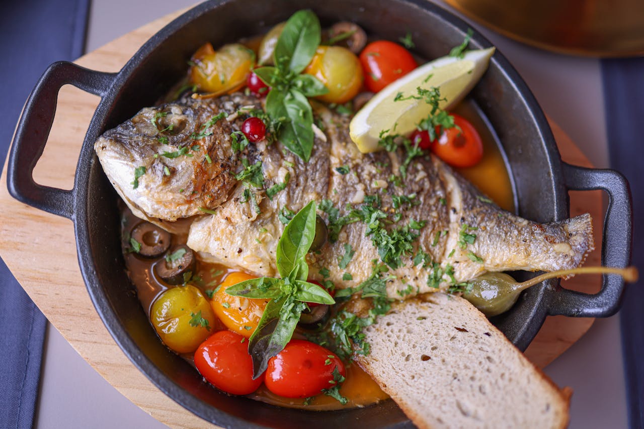Poisson entier grillé servi avec tomates, citron et herbes dans une poêle